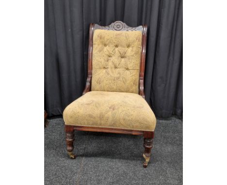 A Victorian dark walnut upholstered button backed chair, with carved floral back rail, turned supports on brass castors, brow
