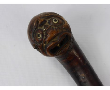 An Antique Walking Stick, the knop carved with an Oriental character with glass eyes and dice in his mouth.