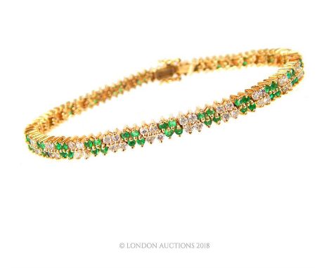 An exquisite, boxed, 14 ct yellow gold, diamond and emerald, tennis bracelet composed of a double row of alternating ninety-t