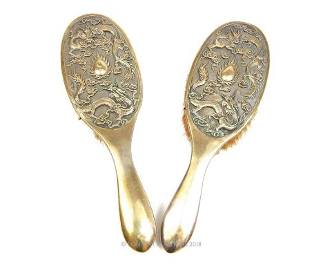 A pair of Chinese silver brushes, decorated in relief with dragons chasing a flaming pearl, stamped with a Chinese mark, 24 x