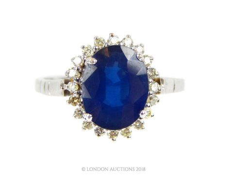 An 18 ct white gold, French, 1960's, sapphire and diamond cluster ring, the central, faceted, four-claw set oval-shaped sapph