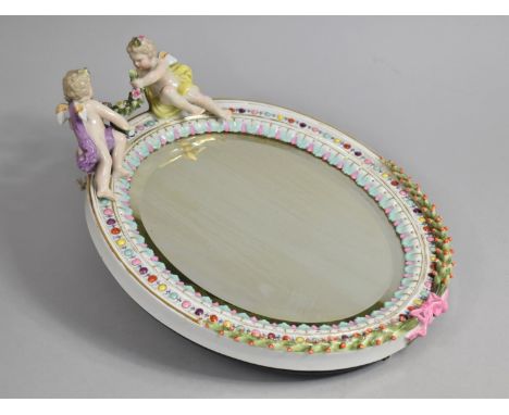 A Porcelain Oval Easel Back Mirror with Polychrome Enamels and Cherub Finials, 28cms High 