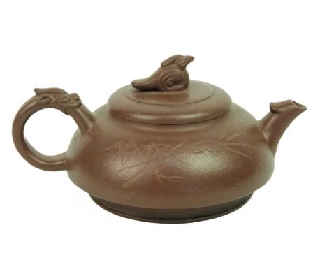 A Chinese Yixing teapot. The cover surmounted by a bird finial above calligraphy opposed by foliage, with dragon mask handle,