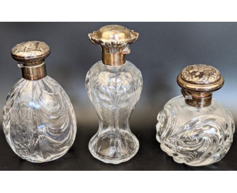 Three Edwardian silver and glass scent bottles by William Comyns, embossed lids depicting angels and figures, all with glass 