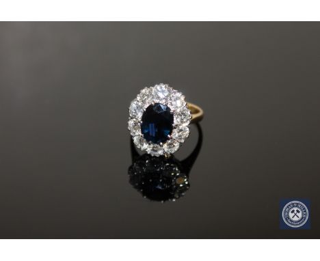 An 18ct gold sapphire and diamond cluster ring, an oval-cut sapphire in a raised claw setting within a border of ten brillian