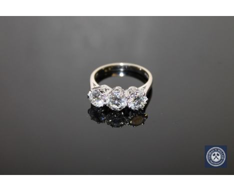 An 18ct white gold three-stone diamond ring, three brilliant-cut stones within raised claw settings, to a plain shank, the to