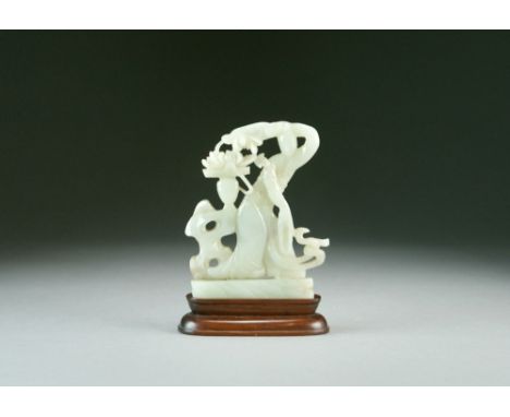 A Chinese pale green jade figure of Guanyin, Qing Dynasty, modelled standing in flowing robes beside a flowering plant atop a