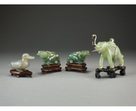 A pair of jadeite figures of water buffalo on carved hardwood stands, each 7cm long, a silver mounted jade figure of an eleph