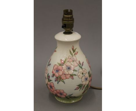 A William Moorcroft pottery lamp base decorated with pink flowers and buds on a green and cream ground. 25 cm high overall.