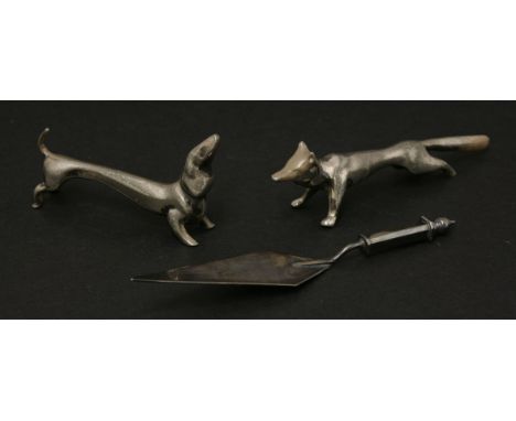 A pair of silver knife rests,in the form of a dachshund and a fox,together with a small silver trowel by Cyril Frost (3)Cyril