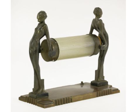 A desk lamp,modelled as two cast figures holding an iridescent cylindrical shade, on a fixed patinated stand,34cm wide30cm hi