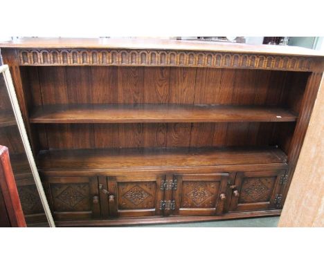 A quality reproduction oak finished storage unit having open shelved upper section over two pairs of carved panel doors   