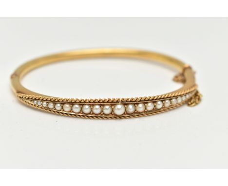 A LATE 19TH CENTURY YELLOW METAL BANGLE, hinged oval bangle, set with twenty one graduated seed pearls and a rope twist borde