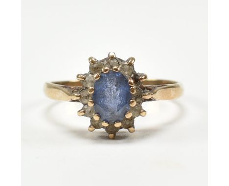 A hallmarked 9ct yellow gold &amp; synthetic sapphire halo ring. The cluster ring having an oval cut pale blue sapphire surro