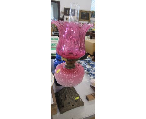 A oil lamp with cranberry shade and oil reserve