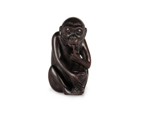 A JAPANESE FRUITWOOD NETSUKE carved as a sitting monkey sucking its finger, holding a peach, signed to base. 5cm high
