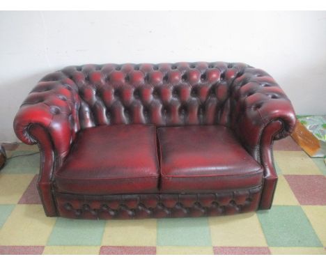 An oxblood red leather button backed two seater chesterfield sofa