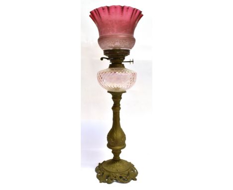 A BRASS BASED OIL LAMP  with clear glass reservoir and cranberry glass shade, 67cm high