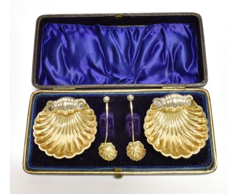 A CASED PAIR OF VICTORIAN SILVER GILT SHELL SALTS AND SPOONS  each on three ball feet, the fluted shell form with gilt interi