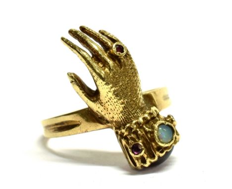 A 9CT GOLD HAND RING  set with a small opal and ruby, the front section of a gloved hand to a yellow gold shank, hallmarked 1