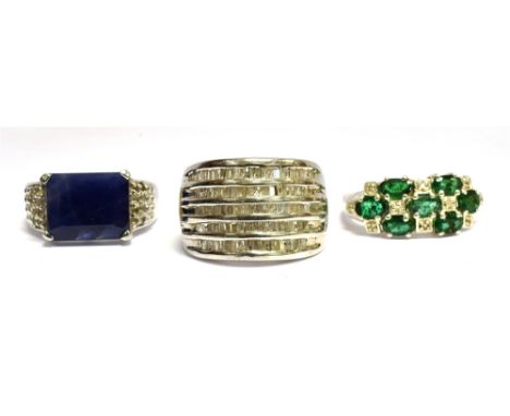 THREE SILVER DRESS RINGS comprising a diamond set five row band ring, an emerald and diamond three row ring and sapphire sing