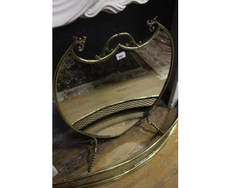 A BRASS AND MIRRORED FIRESCREEN of shield shaped outline with carrying handle raised on splayed legs 77cm (h) x 60cm (w)