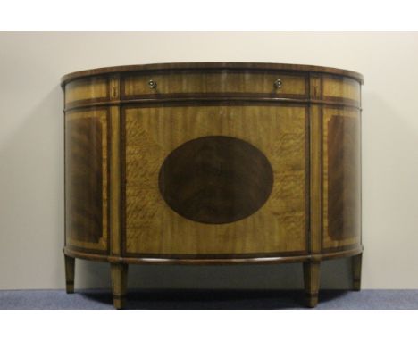 A FINE WALNUT AND SATINWOOD COMMODE of demi-lune outline the shaped moulded top above a frieze drawer and cupboard with oval 