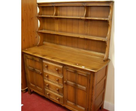 A contemporary Ercol mid-elm dresser, having two-tier plate rack over base fitted with four central long drawers flanked by p