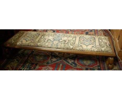 An early 20th century Continental walnut, tapestry embroidered and studded low long footstool, length 123cm