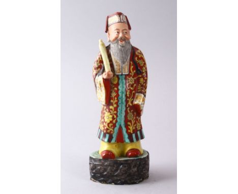 A CHINESE FAMILLE ROSE POTTERY FIGURE OF A SCHOLAR, holding a scroll upon a stylized base, 22cm high.