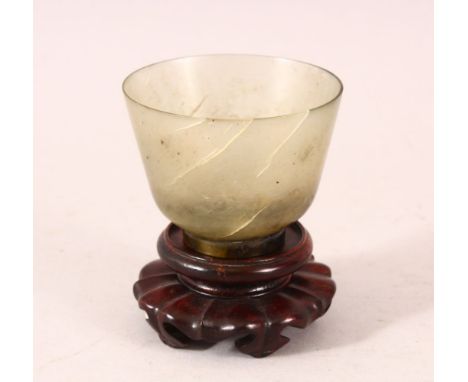 A GOOD JADE CUP on a wooden stand. 2.5ins diameter.