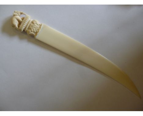 An early 20thC Indian ivory paper knife, having a curved blade, the terminal carved with a standing elephant