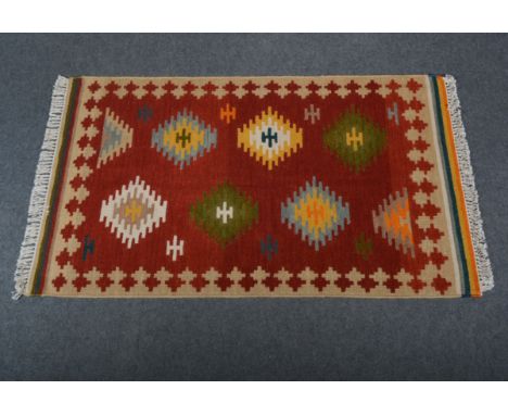Indian rug; with multi-coloured lozenges against a red ground enclosed by sand coloured borders, 90 x 150cm.