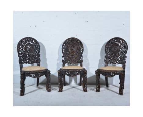 Three Burmese carved hardwood side chairs, cartouche panel backs, upholstered seats on scrolled and mask head legs, height 92