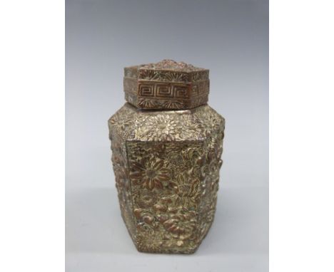 A Japanese embossed metal hexagonal tea caddy decorated with flowers in vases with a Greek key border, 11.5cm tall. 