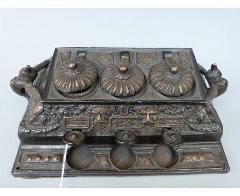 A late 19th/20thC Northern India/Tibetan bronze triple inkwell with push key mechanism to raise the lids, mask decoration and