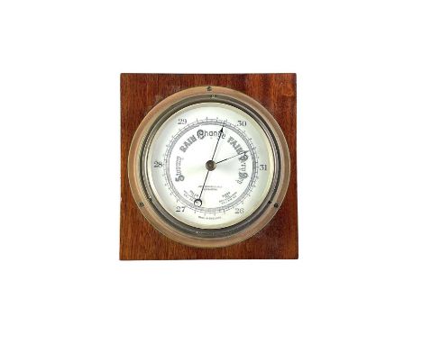 A brass aneroid circular barometer. The white enamel dial signed John Barker &amp; Co, Kensington, on a mahogany plinth, diam