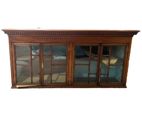 A hanging mahogany bookshelf with dentil cornice over glazed doors before single shelf, 58 x 126 x 30 cm.