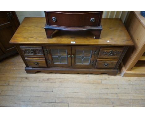 An old charm reproduction oak low side table, having two central leaded light glazed panel doors flanked by four short drawer