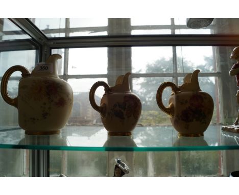 A set of three Royal Worcester ovoid form jugs, all decorated with hand painted floral decoration, with gilt handles.