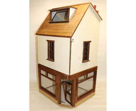 Three-room dolls house modelled as a corner shop, comprising ground floor shop front, room above, and attic room, with wall a