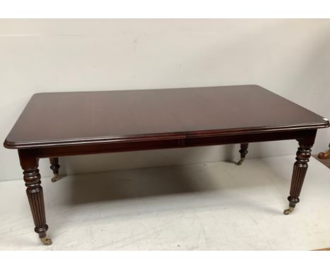 A large reproduction mahogany dining table with additional leaf, raised on turned tapering reeded supports to sabot castors, 