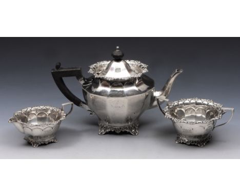 A SILVER THREE PIECE TEA SET, the teapot with twelve panels and cast scroll decoration and matching base with ebonised handle