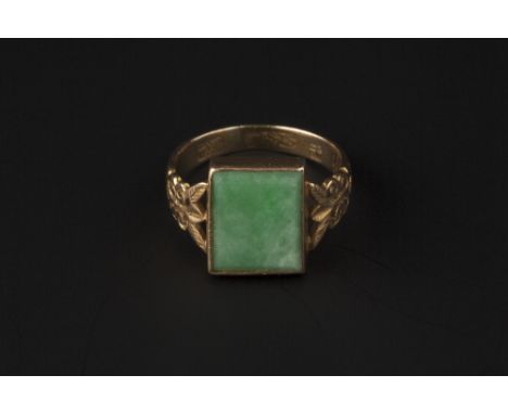 A JADE PANEL RING, the rectangular jade panel collet set between foliate and scroll pierced shoulders, the shank with Orienta