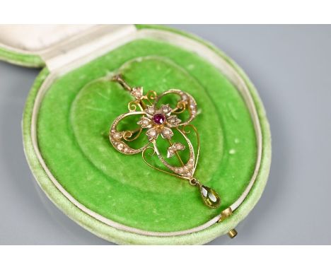 An Art Nouveau flower and scroll open pendant, set overall with seed pearls and with central ruby, with peridot drop below, i