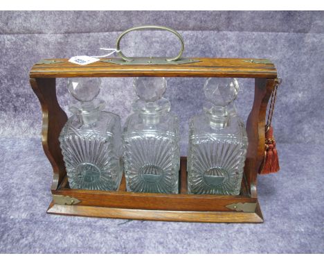 A Tantalus Circa 1920's, with glass spirit decanters, house in oak stand having plated mounts, with key, 36.5cm wide.