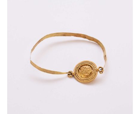 A yellow metal bangle with Gorgonian medallion, possibly Imperial Roman 2nd-4th century AD, with hook fastening, weight appro