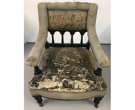 A Victorian ebonised and upholstered armchair on ceramic castors.Turned detail to legs, arm rest supports and spindled back. 