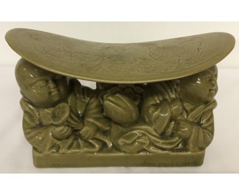A celadon glazed ceramic Chinese pillow.Portraying figures lifting a platform detailing a dragon design.Approx. 12.5cm tall x