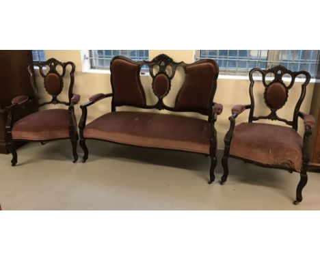 A Victorian 2 seater wooden framed settee with 2 matching arm chairs.With carved detail to seat backs, dark pink velvet uphol